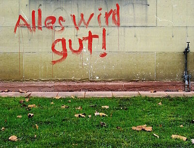 Grafittischriftzug "Alles wird gut" an einer Wand vor grünem Rasen